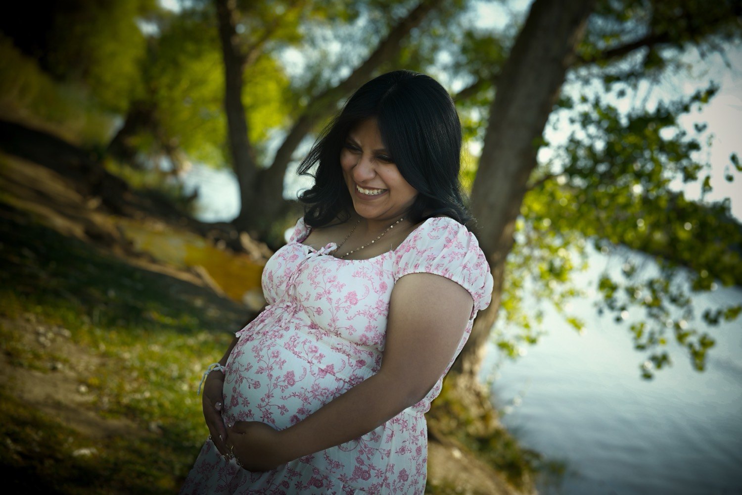 The same woman laughing by the water, both hands held over her belly